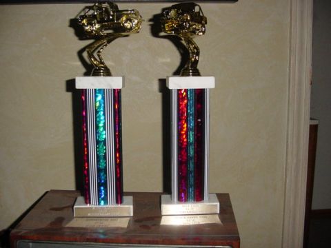 1992 Ford Bronco - Two trophies, each topped with a gold vehicle, are displayed on a table.