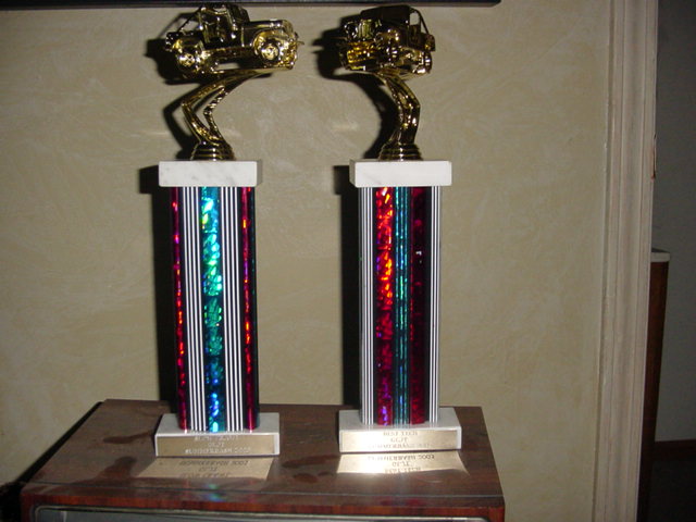 Two trophies with gold vehicle toppers sit on a wooden surface
