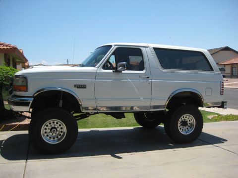 1996 Ford Bronco - This lifted Ford Bronco is parked on a paved surface with a residential area in the background.