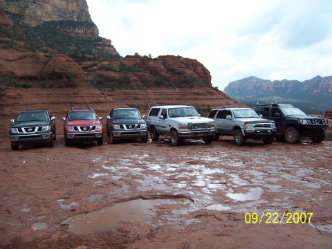 1996 Ford Bronco - A group of SUVs are parked on a wet, red rock surface with a scenic mountain backdrop.