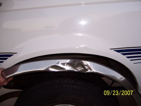 1996 Ford Bronco - Damage to the fender and chrome trim around the wheel well of a white vehicle is visible.