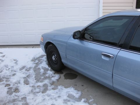 1999 Ford Crown Victoria - A light blue sedan is parked in front of a garage door with snow on the ground.