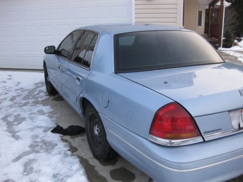 1999 Ford Crown Victoria - A light blue sedan is parked in front of a garage with snow and ice on the ground.