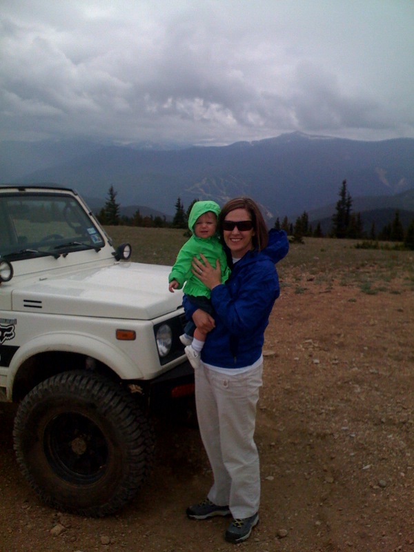 1987 Suzuki Samurai parked on dirt with woman holding baby, mountains in background