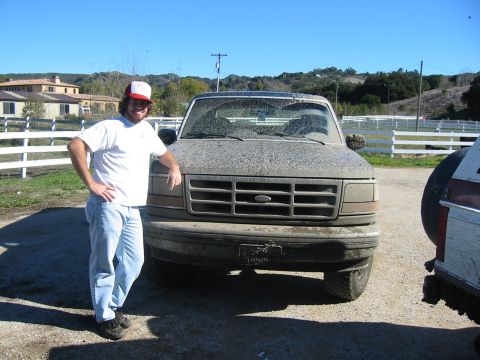 1993 Ford Bronco - A man poses next to a heavily soiled Ford truck, partially obscuring another vehicle on the right.