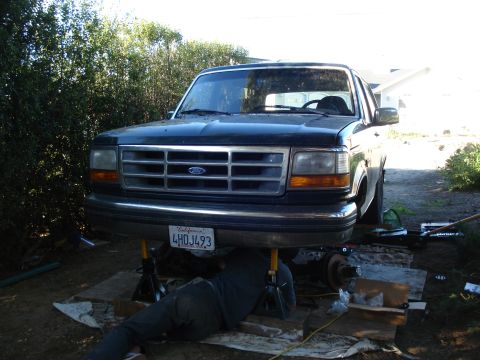 1993 Ford Bronco - A 1993 Ford Bronco is raised on jack stands, with a mechanic working underneath it.