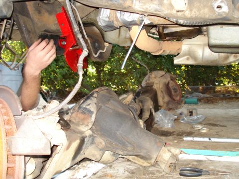 1993 Ford Bronco - Mechanic works on the underbody of a vehicle, focusing on suspension and drivetrain components.