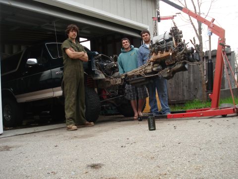 1993 Ford Bronco - An engine is being removed from a black SUV with the help of an engine hoist and three people.