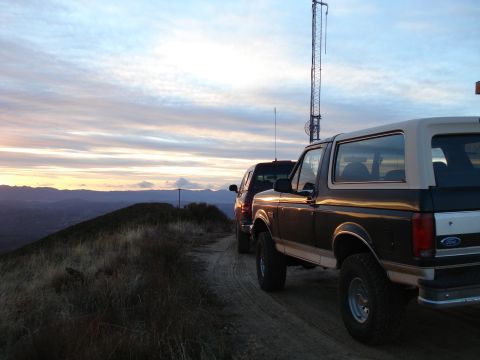 1993 Ford Bronco - Two SUVs, including a 1993 Ford Bronco, are parked on a dirt road overlooking a valley at sunset.