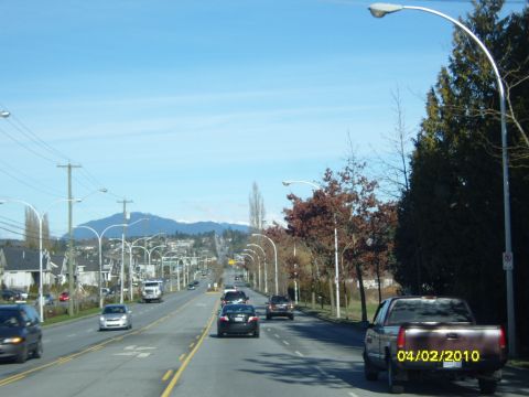 1989 Ford Bronco - A street scene with multiple vehicles under a clear blue sky, with mountains in the distance.