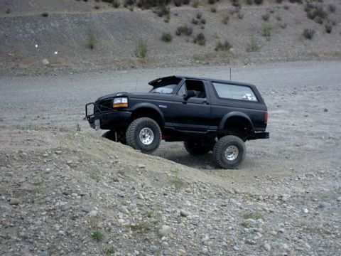 1995 Ford Bronco - A modified black Ford Bronco navigates a rocky incline on a dirt road.