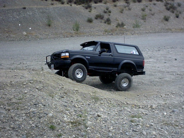Black lifted two-door Ford Bronco with brush guard climbing dirt mound in gravel pit