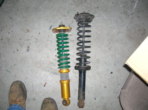 1987 Mazda RX-7 - Comparison of two car shock absorbers, one aftermarket and one stock, on a concrete surface.