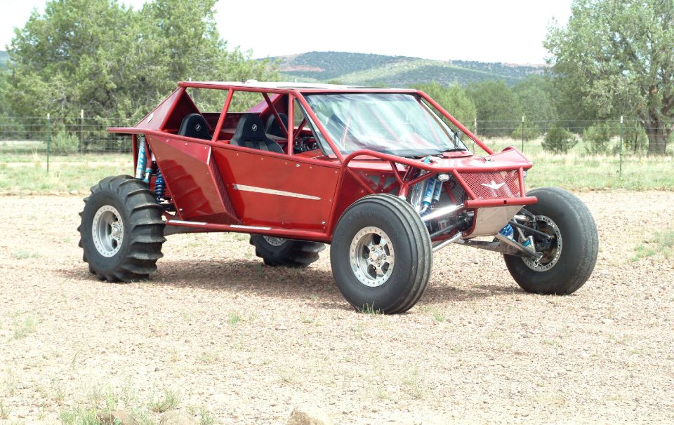Red tube-chassis off-road buggy with paddle tires in a dirt field