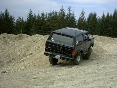 1995 Ford Bronco - A black 1995 Ford Bronco navigates a dirt hill, its off-road capabilities.