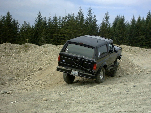 Black Ford Bronco SUV climbing dirt mound at off-road site