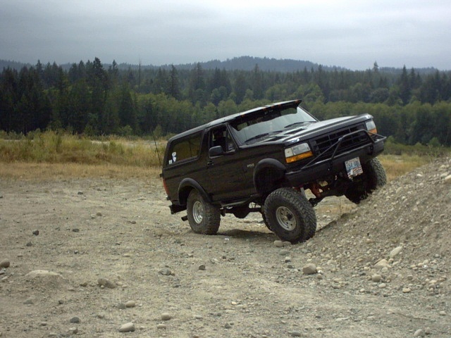 Black lifted two-door Ford Bronco climbing a dirt mound off-road