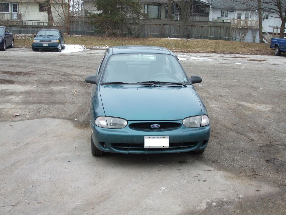 Teal 1997 Ford Aspire sedan, front view, parked on gravel lot