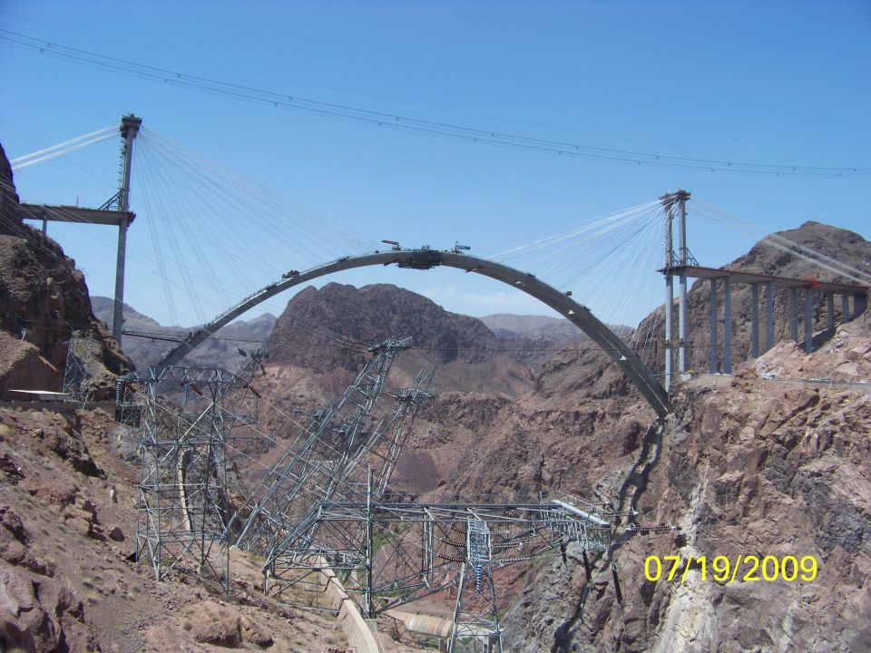 Bridge construction with steel arch and suspension towers over a rocky canyon