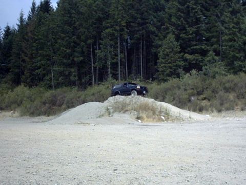1995 Ford Bronco - A dark SUV is positioned on a dirt pile in a wooded area.