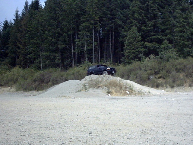 Dark SUV parked on a gravel mound in front of evergreen forest
