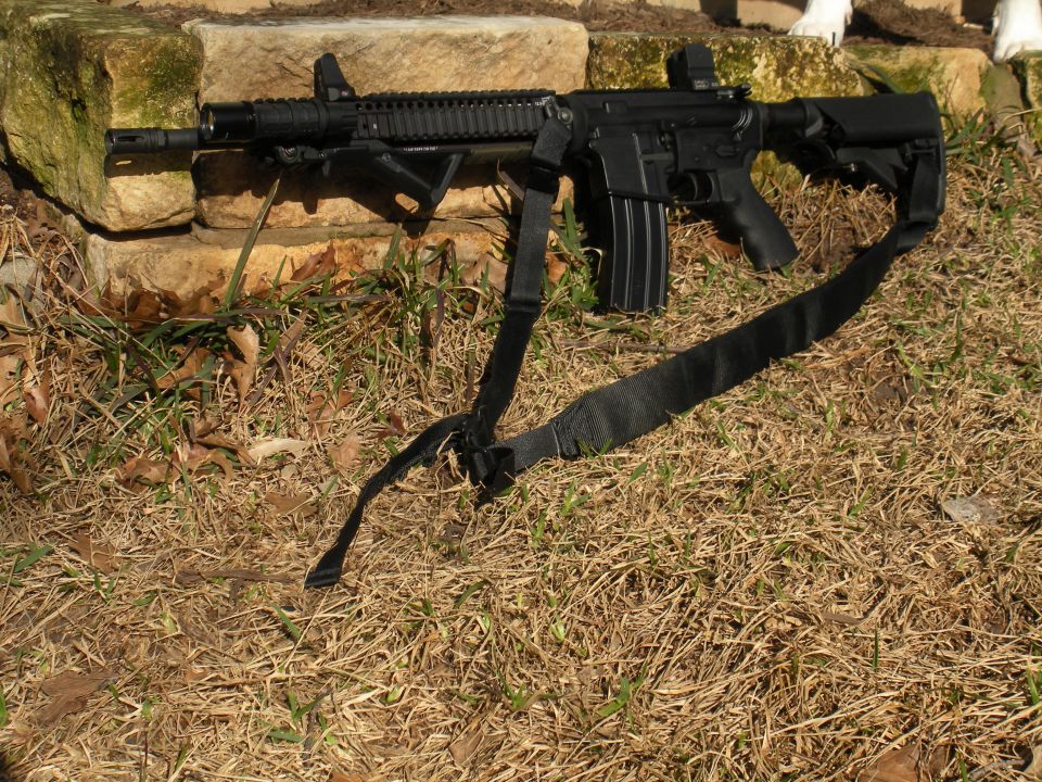 Black rifle with sling and bipod resting on grass and stones