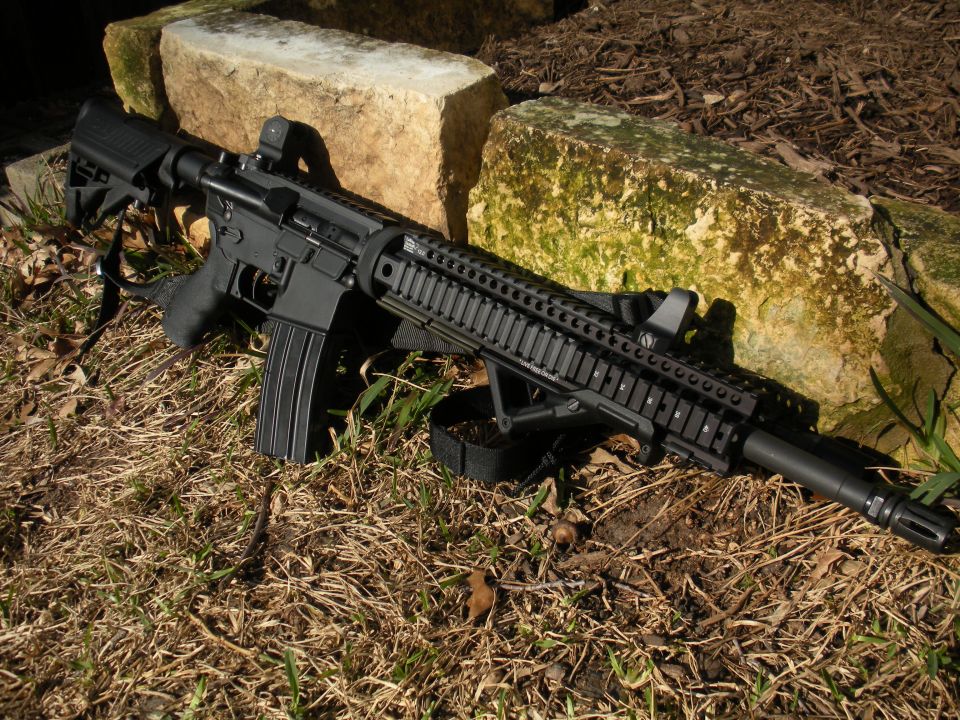 Black rifle with red dot sight resting on grass and rocks