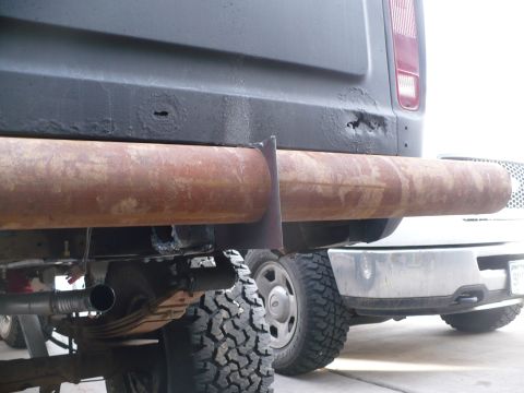 1979 Ford Bronco - Close-up of a heavily rusted pipe rear bumper, showing exhaust components and leaf springs on a dark-colored vehicle.