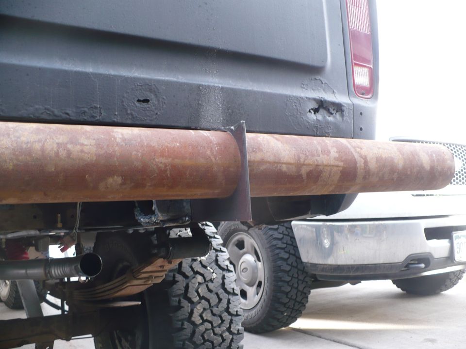 Rusty pipe rear bumper with visible exhaust and leaf springs on a dark vehicle