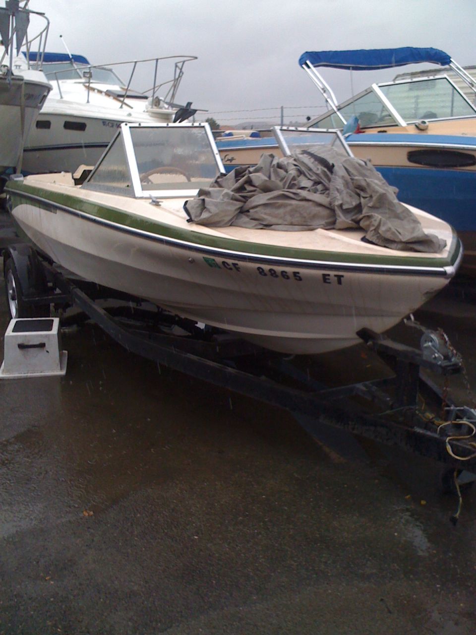 White and green fiberglass bowrider on a trailer in a rainy boat storage yard
