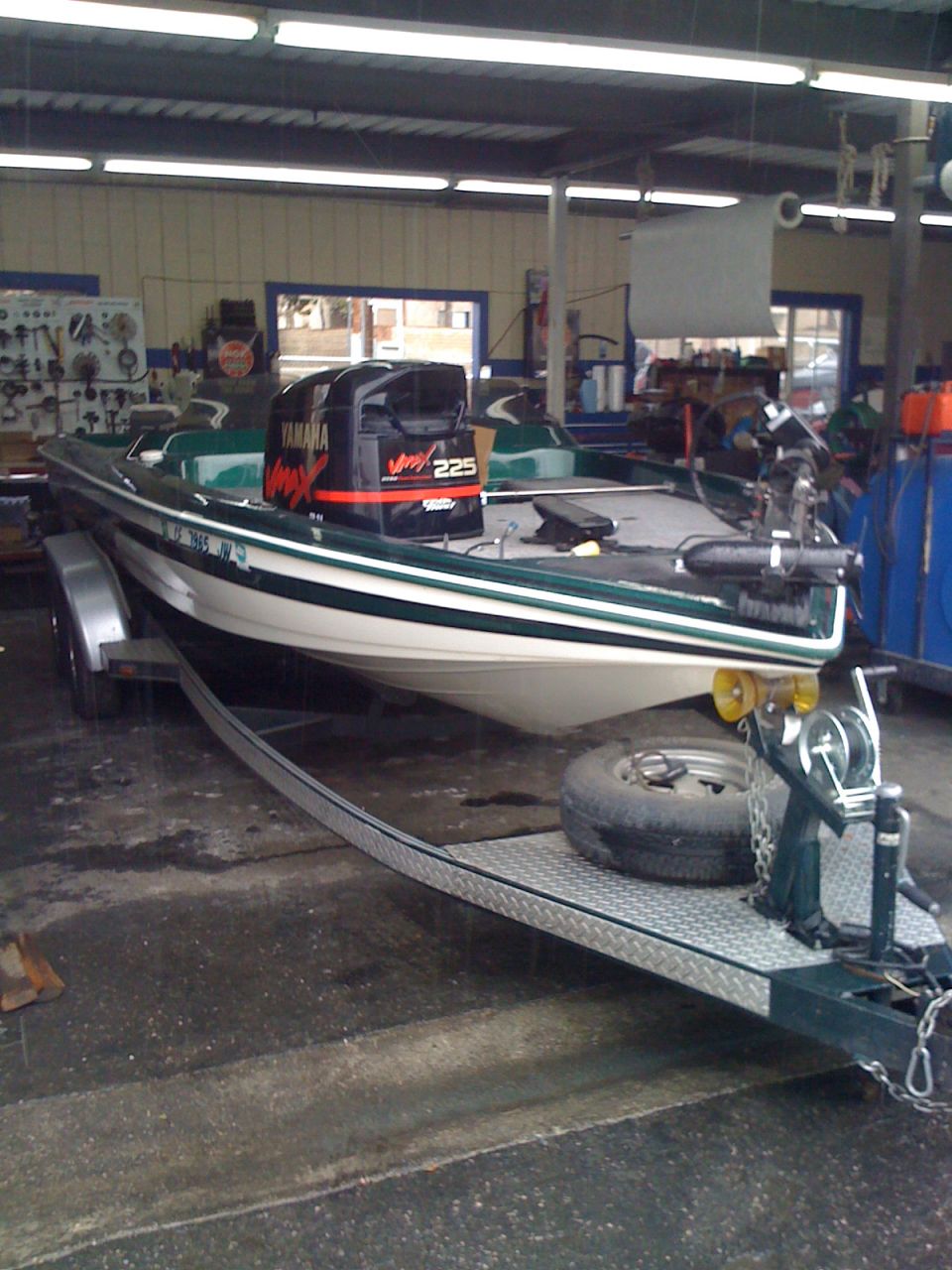 Green and white bass boat on trailer with Yamaha VMAX 225 outboard in a shop