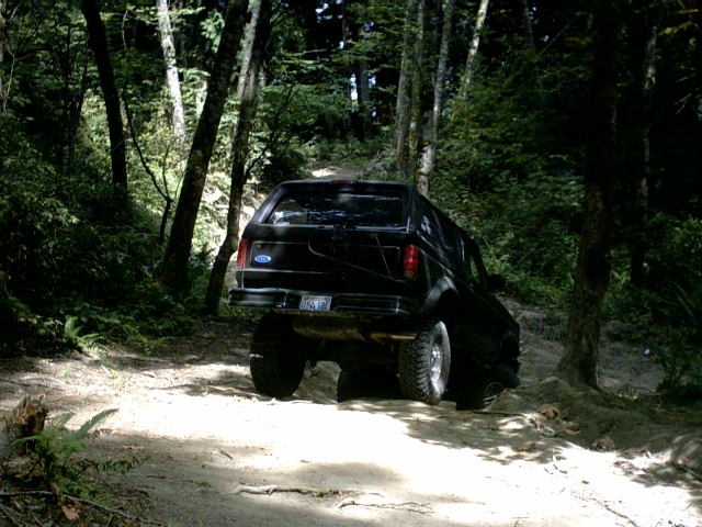 Black lifted Ford SUV climbing a dirt trail in the woods, rear view