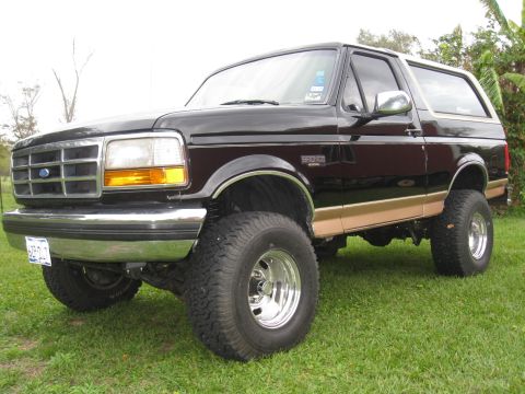 1994 Ford Bronco - This lifted Ford Bronco is parked on a grassy lawn with trees in the background.