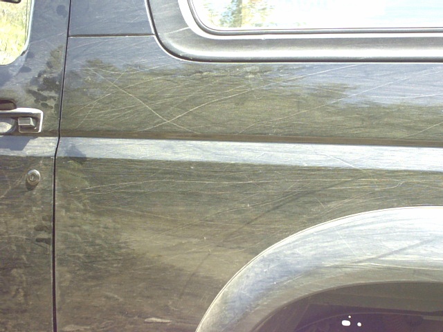 Dark green vehicle door and quarter panel covered in swirling scratches