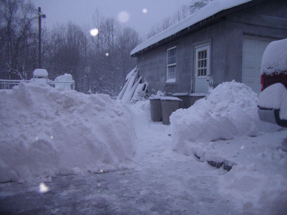 Rear of a red vehicle partially covered in snow next to a building during a snowstorm