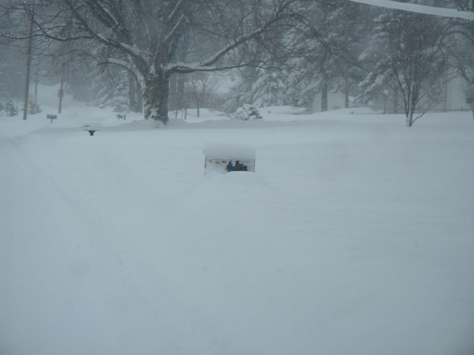 Snowmobile partially buried in snow in a yard during a blizzard