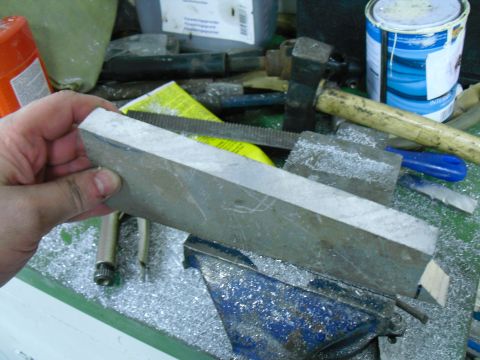 1996 Ford Bronco - A metal part is held in a vise, with various tools and materials scattered around the workbench.