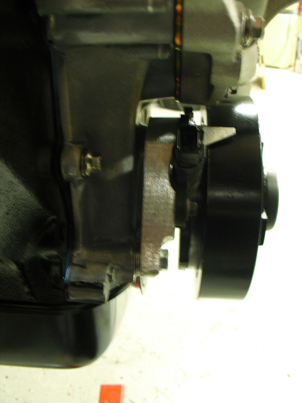 Close-up of machined metal bracket bolted to black-painted engine or transmission casting