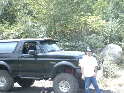 1995 Ford Bronco - A black Ford Bronco with aftermarket modifications is shown from a 3/4 front angle, with a man standing next to it.