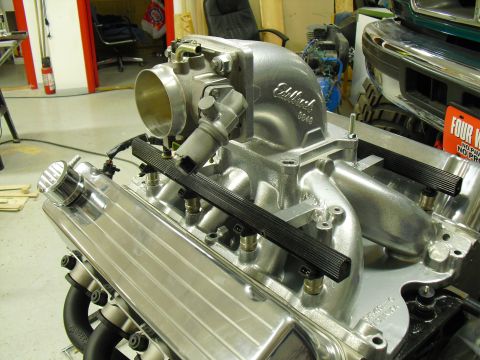 1996 Ford Bronco - The engine's intake manifold and fuel rail system are shown in detail, with a portion of a green truck visible in the background.