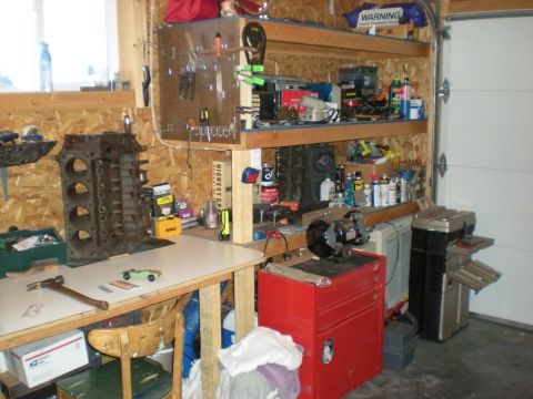 1974 Ford Ranchero - A cluttered garage workbench displays an engine block, tools, and supplies, with a garage door in the background.