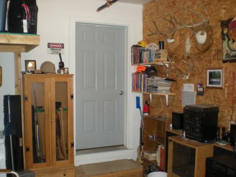 1974 Ford Ranchero - A cluttered garage interior features a gray door, storage cabinets, shelves filled with books and hunting trophies, and various tools.