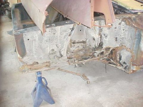 1970 Ford Mustang - Car frame undergoing restoration, supported by jack stands. Visible rust and structural components.