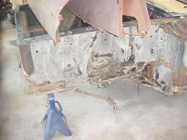 rusted car frame on blue jack stands, showing suspension components and body mounts