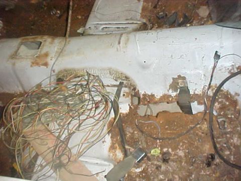 1970 Ford Mustang - A close-up view of a damaged car interior, showing extensive rust and a large amount of loose wiring.