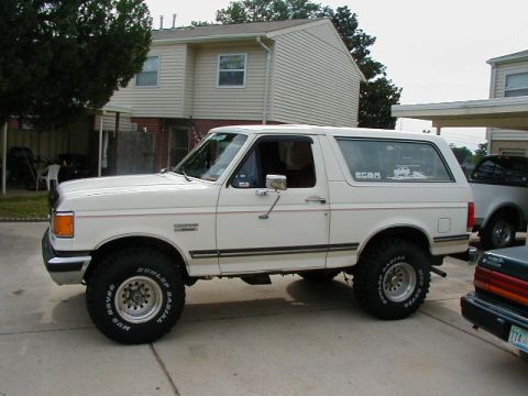 1990 Ford Bronco - This white Ford Bronco is parked in a residential driveway next to another vehicle.