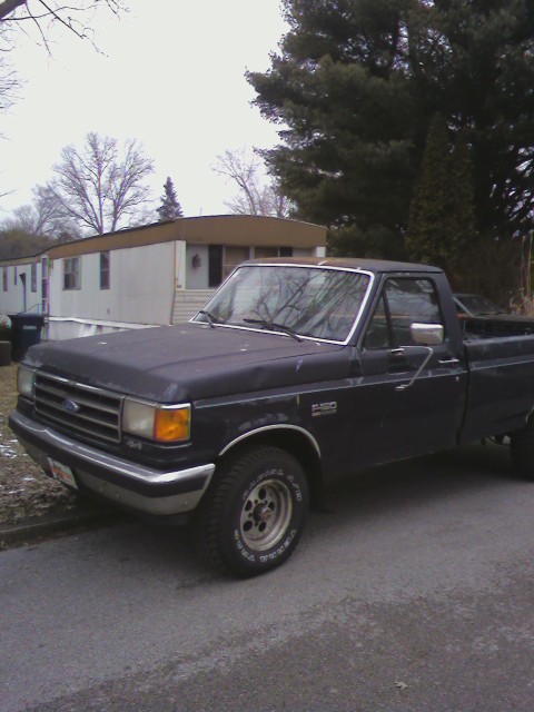 1991 Ford F-150 - A dark blue 1991 Ford F-150 pickup truck is parked on the side of the road with a trailer home behind it.