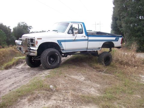 1982 Ford F-100 - This lifted pickup truck has off-road tires and an aftermarket bumper, seen on uneven terrain.