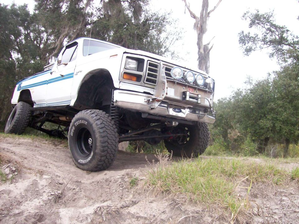 White pickup truck with blue stripe, lifted suspension, and off-road tires on a dirt incline