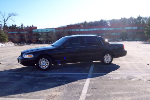 2001 Ford Crown Victoria - A black 2001 Ford Crown Victoria is parked in a lot with a large building in the background.